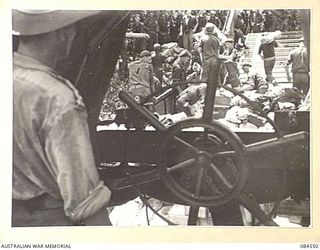 JABA RIVER AREA, BOUGAINVILLE, SOLOMON ISLANDS. 1944-12-18. THE HELMSMAN, (FOREGROUND), ABOARD A BARGE TRANSPORTING B COMPANY, 15 INFANTRY BATTALION SOUTH OF THE RIVER TO TAKE UP NEW POSITIONS