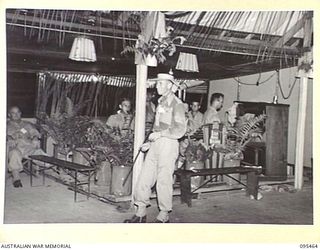 LAE AREA, NEW GUINEA, 1945-08-22. WARRANT OFFICER 2 N.T. TODD, MASTER OF CEREMONIES, IN FRONT OF THE LAE BASE ORCHESTRA DURING THE MASKED MYSTERY BALL HELD AT NO. 3 SERGEANT'S MESS, HEADQUARTERS ..