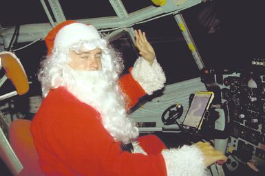 Santa Claus (SSGT Michael Kunch) waves from the pilot's seat of a C-130 Hercules aircraft. Donated Christmas gifts collected by volunteers from the 43rd Security Police Squadron, the 605th Military Airlift Support Squadron, and the 43rd Munitions Maintenance Squadron are being parachuted onto local islands