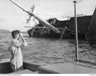 PORT MORESBY, PAPUA. C. 1944. A CREW MEMBER OF A MOTOR LAUNCH OF THE RAAF RESCUE SERVICE LOOKS AT THE WRECK OF THE MV MACDHUI WHICH WAS THE TARGET OF ATTACKS BY JAPANESE BOMBER AIRCRAFT ON ..