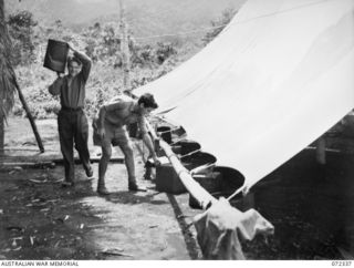 EFOGI, NEW GUINEA. 1944-04-07. SIGNALMAN H.J. YOUNG (1), AND VX119475 SIGNALMAN A.A. MCNAMARA (2), MEMBERS OF THE 23RD LINE SECTION, 18TH LINES OF COMMUNICATION SIGNALS, COLLECT WATER CAUGHT FROM A ..