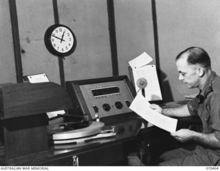 PORT MORESBY, PAPUA, NEW GUINEA, 1944-01-31. GEOFFREY F. NORTON, FORMERLY OF THE 6TH DIVISION, AUSTRALIAN ARMY SERVICE CORPS, READING THE NEWS FROM THE ANNOUNCER'S DESK AST 9PA, THE AUSTRALIAN ..