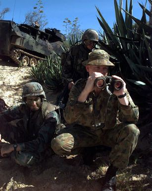 Royal Australian Navy Captain Chris G. E. Cowler (foreground) joins US Marine Corps Lieutenant Chris Budihas (left) and US Marine Corps Lance Corporal Gil Ducy (back) in observing assault activities during an amphibious assault at Pacific Missile Range Facility, Barking Sands, Kauai, Hawaii, during RIMPAC '96