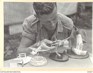 LAE AREA, NEW GUINEA. 1945-06-03. DURING AN EXHIBITION OF HOBBIES AND CRAFTS PRIVATE N.G. ANDERSON ADMIRES PERSPEX PLANES MODELLED BY MEN AT 112 CONVALESCENT DEPOT