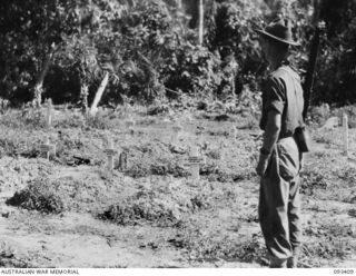 WEWAK AREA, NEW GUINEA. 1945-06-27. AN AUSTRALIAN SOLDIER, A MEMBER OF HEADQUARTERS 6 DIVISION READING THE HEADBOARDS IN A SMALL CEMETERY THAT STANDS AT THE SIDE OF BIG ROAD, THE ROAD TO GO THROUGH ..