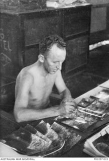 Madang, New Guinea, 1945. Flying Officer (FO) Gene McCarthy, Photograph Intelligence Officer at Headquarters, RAAF Northern Command (NORCOM), working at his desk. With the aid of a stereoscopic ..