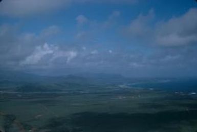 [Aerial view of green fields stretching to a coast with distant mountains on Kauai Island, United States]