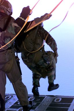 Rear view medium close up shot from the rear entrance of a USAF C-130 Hercules Cargo aircraft at US Marines from Company A, 5th Reconnaissance Battalion, 3rd Marines, as they jump from the plane with their MC5 Static Line Square Parachutes and 100-pound All Purpose, Light, Weight, Individual Carrying Equipment (ALICE) packs to the ground after performing a 6-thousand foot combat jump during Force Reconnaissance Exercises over Andersen Air Force Base, Guam