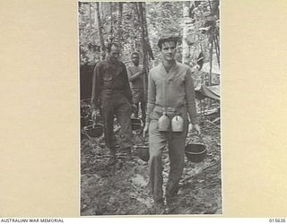 1943-08-30. NEW GUINEA. AMERICAN SOLDIERS WALKING THROUGH THE MUD ON MOUNT TAMBU WITH SUPPLIES OF WATER FOR THEIR MATES FURTHER UP THE MOUNTAIN SIDE. THEIR STEEL HELMETS ENABLE THEN TO CARRY WATER ..