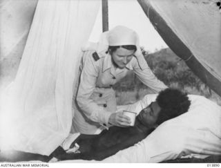 1942-12-18. NEW GUINEA. SENIOR SISTER J. WHEATLEY, RAAF NURSING SERVICE, AT AN RAAF MEDICAL RECEIVING STATION GIVES A DRINK TO A NATIVE BOY NAMED LAURABURI (WHICH MEANS WHITE CLOUD) WHO WAS ..