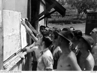 PORT MORESBY, PAPUA. C. 1944-05. MEMBERS OF THE RAAF AIRCRAFT REPAIR DEPOT READING A WALL NEWSPAPER