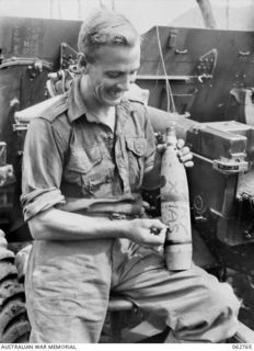 RAMU VALLEY, NEW GUINEA. 1943-12-25. VX54822 GUNNER A. W. BRIGHT OF "C" TROOP, NO. 8 BATTERY, 2/4TH FIELD REGIMENT WRITING MERRY CHRISTMAS ON A 25 POUNDER SHELL WHICH WILL BE SHOT OVER INTO THE ..