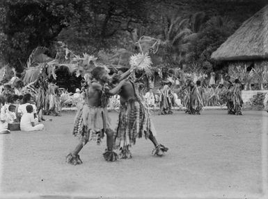 [Pacific island men performing to seated individuals]