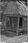 Carving: M'lapokala carving a wooden bowl with a stand, probably for tourist trade, he sits on veranda of a small house