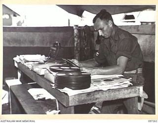 CAPE WOM, NEW GUINEA. 1945-09-29. CORPORAL F.R. SAWYER AT RADIO 6 DIVISION, HEADQUARTERS 6 DIVISION, SELECTING RECORDS FROM THE STATION'S RANGE FOR THE REQUEST SESSION. THE STATION REOPENED ON 6 ..