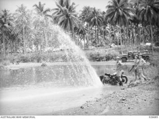 MILNE BAY, PAPUA. 1942-10. AN AUSTRALIAN DESPATCH RIDER WHOSE MOTOR-CYCLE BECAME WEDGED BETWEEN TWO ROCKS WHEN CROSSING A RIVER IN THE GILI GILI AREA, THROWS UP A STREAM OF WATER FROM THE ..
