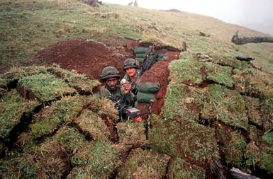 SPEC. 4 Herman Morris Jr., in a foxhole with SPEC. 4 Charles G. King, holds up a Tropic Lightning gold coin given to him by Brig. Gen John T. Quinn during training Exercise OPPORTUNE JOURNEY 4-83. Both men are members of Company C, 1ST Battalion, 21st Infantry, 25th Infnatry Division