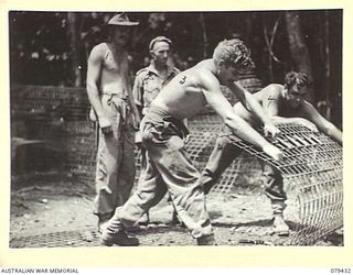 MEVELO RIVER, HENRY REID BAY, NEW BRITAIN. 1945-03-05. SAPPERS OF THE 4TH FIELD COM0PANY, ROLLING ARC MESH FOR PIERS DURING THE BUILDING OF A BRIDGE OVER THE RIVER. IDENTIFIED PERSONNEL ARE: ..