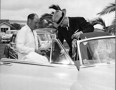 Former President Truman standing as he exits a convertible car after being greeted by an unidentified man