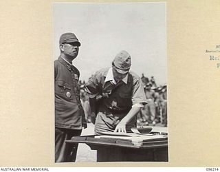 CAPE WOM, NEW GUINEA, 1945-09-13. JAPANESE INTERPRETER READING THE SURRENDER TERMS TO LIEUTENANT-GENERAL ADACHI, COMMANDER 18TH JAPANESE ARMY IN NEW GUINEA. LIEUTENANT-GENERAL ADACHI FORMALLY ..