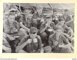 ILIPEM, NEW GUINEA, 1945-07-31. MEMBERS OF 11 PLATOON, 2/5 INFANTRY BATTALION, ENJOYING THEIR FOOD. ALL FOOD IS DROPPED BY KAI BOMBERS AND OFTEN PREPARED WITH THE JAPANESE DEFENSIVE POSITIONS IN ..