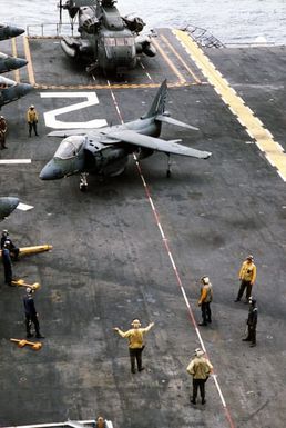 A plane director signals to the pilot of an AV-8B Harrier aircraft taxiing on the flight deck of the amphibious assault ship USS SAIPAN (LHA-2) during a rehearsal for Operation Sharp Edge. The SAIPAN is on station off the coast of Liberia