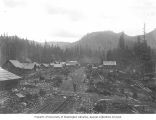 Man standing on railroad tracks with cabins on either side, Detroit, Oregon, between 1895 and 1905