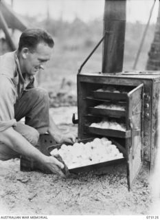 ALEXISHAFEN, NEW GUINEA. 1944-05-11. N452914 PRIVATE H.G. WOODROFF, A MEMBER OF THE 30TH INFANTRY BATTALION, 8TH INFANTRY BRIGADE, PLACING POTATOES IN AN OVEN TO ROAST. THE POTATOES, FRESHLY ARRIVE ..