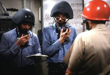 Members of a damage control team, wearing protective helmets, relay information from a firefighting party chief petty officer by means of sound-powered phones as they take in a firefighting drill aboard the amphibous assault ship USS GUAM (LPH 9)