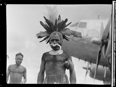 Unidentified local man [cheif?] at Kerowagi airfield, Papua New Guinea, featuring traditional adornments including nose-piercing, headdress, and shell necklace