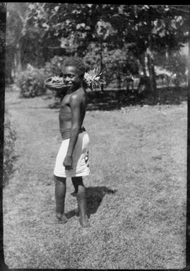 Member of Government House staff holding a bowl of fruit on his shoulder, Rabaul, New Guinea, ca. 1929, 2 / Sarah Chinnery