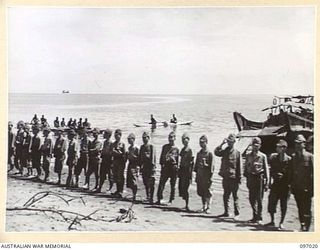 1945-09-19. NATIVES IN CANOES LOOK ON AT JAPANESE SOLDIERS LINING THE BEACH. THE SICK AND WOUNDED ARE AWAITING EVACUATION FROM NUMA NUMA TO TOROKINA. A JAPANESE LANDING BARGE IN RIGHT BACKGROUND. ..