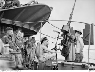 Members of the 25th Infantry Battalion watching the gun crew at practice aboard the RAN frigate, HMAS Barcoo as the vessel proceeds from Siar to Potsdam. Identified are (left to right): QX61399 ..