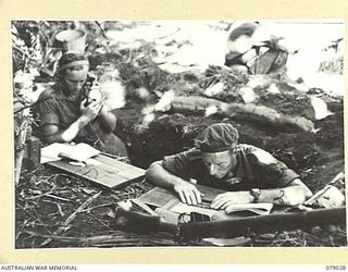 TSIMBA RIDGE, BOUGAINVILLE ISLAND. 1945-02-06. NX161744 LIEUTENANT E.A TUCKWELL, SECOND- IN- CHARGE, 101ST BRIGADE SUPPORT COMPANY, CHECKING ROUNDS AND REPORTS IN HIS SLIT TRENCH DURING AN ACTION ..