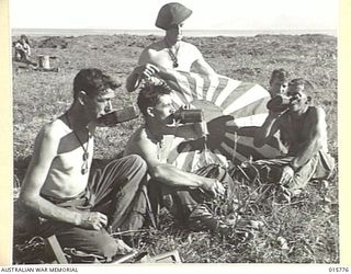 1943-09-22. NEW GUINEA. AUSTRALIAN TROOPS CAPTURE LAE. MEN FROM WESTERN AUSTRALIAN AND VICTORIAN UNITS REST BESIDE A JAPANESE HEADQUARTERS FLAG AT LAE. LEFT TO RIGHT - PTES. DAVID INGRAM, HAROLD ..