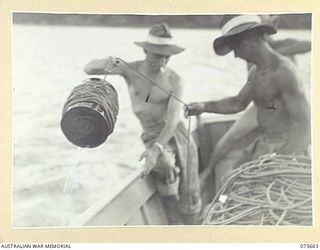 SALAMAUA, NEW GUINEA. 1944-06-02. N290472 PRIVATE S.E. CHAPMAN, 2ND MARINE FOOD SUPPLY PLATOON (2), ASSISTED BY Q271745 CRAFTSMAN C.D. HANDFORD (1), HAULS A BUOY ABOARD ONE OF THE PLATOON'S ..