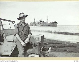 LAE, NEW GUINEA. 1944-07-05. NX134772 WARRANT OFFICER I, H. REID, CHIEF CLERK, DEPUTY DIRECTOR OF ORDNANCE SERVICES, NEW GUINEA FORCE, SEATED ON THE FRONT MUDGUARD OF HIS JEEP. IN THE BACKGROUND AN ..