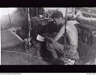 MARKHAM VALLEY AREA, NEW GUINEA. C.1945. SERGEANT N. (NAT) F. DANIELL OF THE MOBILE PROPAGANDA UNIT, FAR EASTERN LIAISON OFFICE, IN HIS TENT LISTENING TO AN AUSTRALIAN RADIO BROADCAST TO BE USED IN ..