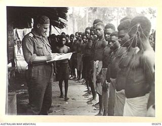 BOUGAINVILLE. 1945-05-30. CAPTAIN R. ORMSBY, ANGAU DISTRICT SERVICES (1), CHECKING THE NAMES OF APPLICANTS FROM THE NARGOVISSI TRIBE AT MARAU REFUGEE CAMP. THEY RECEIVE A MEDICAL INSPECTION BEFORE ..