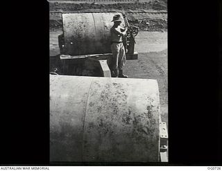 NADZAB, NEW GUINEA. C. 1944-02. LEADING AIRCRAFTMAN M. E. SELWOOD, ORANGE, NSW, LOOKING AT HEAVY SIX TON ROLLERS USED BY NO. 62 MOBILE WORKS SQUADRON RAAF TO ROLL OUT GROUND TO BE USED AS A BOMBER ..