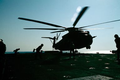 Flight deck crewmen aboard the amphibious assault ship USS GUAM (LPH 9) move toward a CH-53 Sea Stallion helicopter with wheel chocks, as it touches down during operations off the coast of Beirut, Lebanon