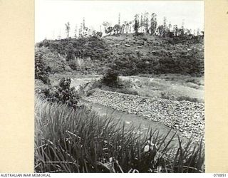 WAU - LAE ROAD, NEW GUINEA, 1944-02-20. AN OLD MINING VILLAGE ON THE SLOPE OF A HILL SIX MILES FROM WAU. THE BULOLO RIVER IS BANKED WITH TAILINGS FROM THE DREDGE