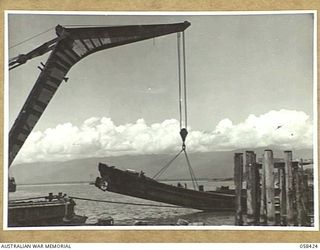 LAE, NEW GUINEA, 1943-10-13. CRANE OF THE UNITED STATES SMALL SHIPS SECTION RAISING A SUNKEN JAPANESE BARGE FROM THE DOCK AREA