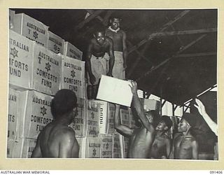 JACQUINOT BAY, NEW BRITAIN, 1945-04-28. NATIVE BOYS STACKING MID-YEAR PARCELS OF COMFORTS IN THE AUSTRALIAN COMFORTS FUND STORE