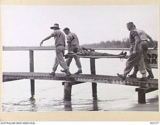 BOUGAINVILLE, 1945-06-18. MEMBERS OF 1 WATER AMBULANCE CONVOY, CARRYING A NATIVE STRETCHER CASE ALONG A JETTY TO A WAITING BOAT, DURING THE EVACUATION OF WOUNDED BY WATER FROM MOTUPENA POINT, ..