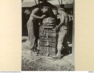 TOROKINA, BOUGAINVILLE ISLAND. 1945-01-29. PRIVATE W. HIGGINS (1) AND WARRANT OFFICER I A. BRUN (2) SOLOMON'S DETACHMENT, 12TH AIR MAINTENANCE PLATOON, 4TH BASE SUB AREA, ATTACHING A PARACHUTE TO A ..