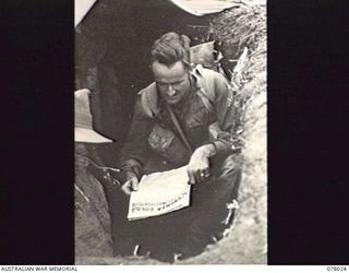 BOUGAINVILLE ISLAND. 1944-12-30. Q22312 PRIVATE R. KEEN, 25TH INFANTRY BATTALION, READING "GUINEA GOLD", THE AUSTRALIAN ARMY NEWSPAPER, IN HIS DUGOUT WHILE WAITING FOR THE ORDER TO ADVANCE AGAINST ..