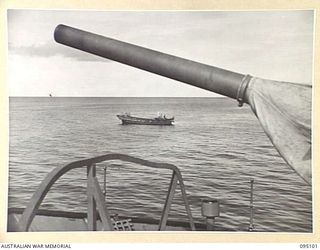 AT SEA, OFF BUIN, BOUGAINVILLE, 1945-08-20. A 4-INCH GUN ON THE BOW OF HMAS LITHGOW STANDS SILENT SENTRY AS A JAPANESE BARGE LAYS OFF THE CORVETTE WHILE NEGOTIATIONS ARE BEING CARRIED OUT BY ..