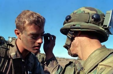 Sergeant Robert Gibson, Company A, applies camouflaged paint to the face of Private First Class Dennis Gordon. The men, both members of the 2nd Brigade, 25th Infantry Division, are preparing for an airmobile assault during training Exercise OPPORTUNE JOURNEY 4-83