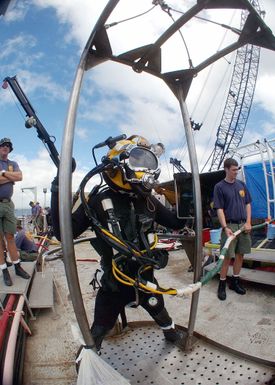 A US Navy diver assigned to Mobile Diving and Salvage Unit One (MDSU-1), wearing a full diving suite, stands aboard a diving stage, aboard the Crowley 450-10 barge during recovery operations for the Japanese fishing vessel Ehime Maru off the coast of Hawaii